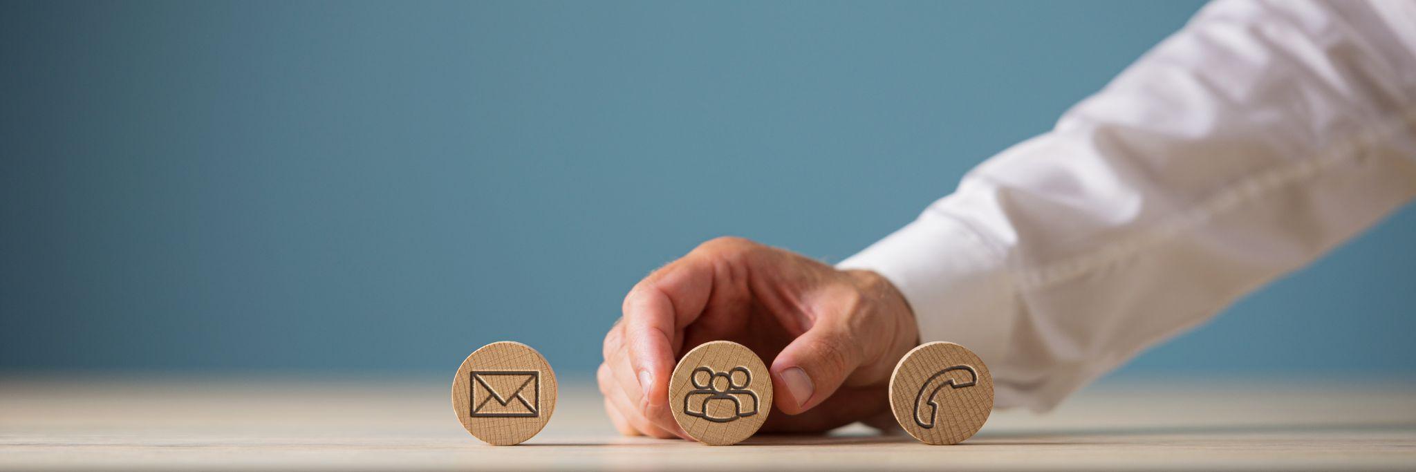 customer service representative placing three wooden cut circles with contact and information icons on them in a row.