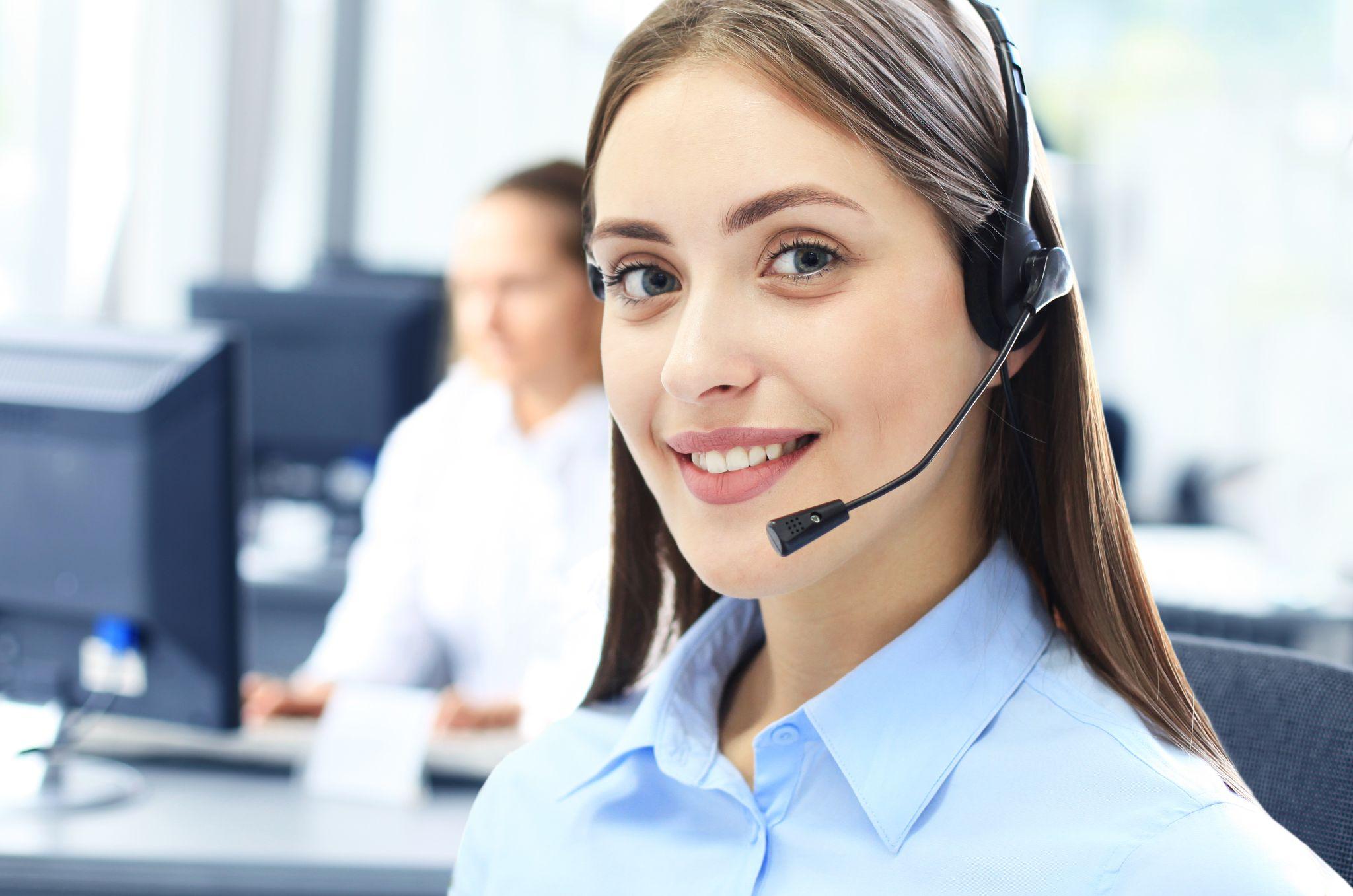 Beautiful young female call center operator with headset in office.