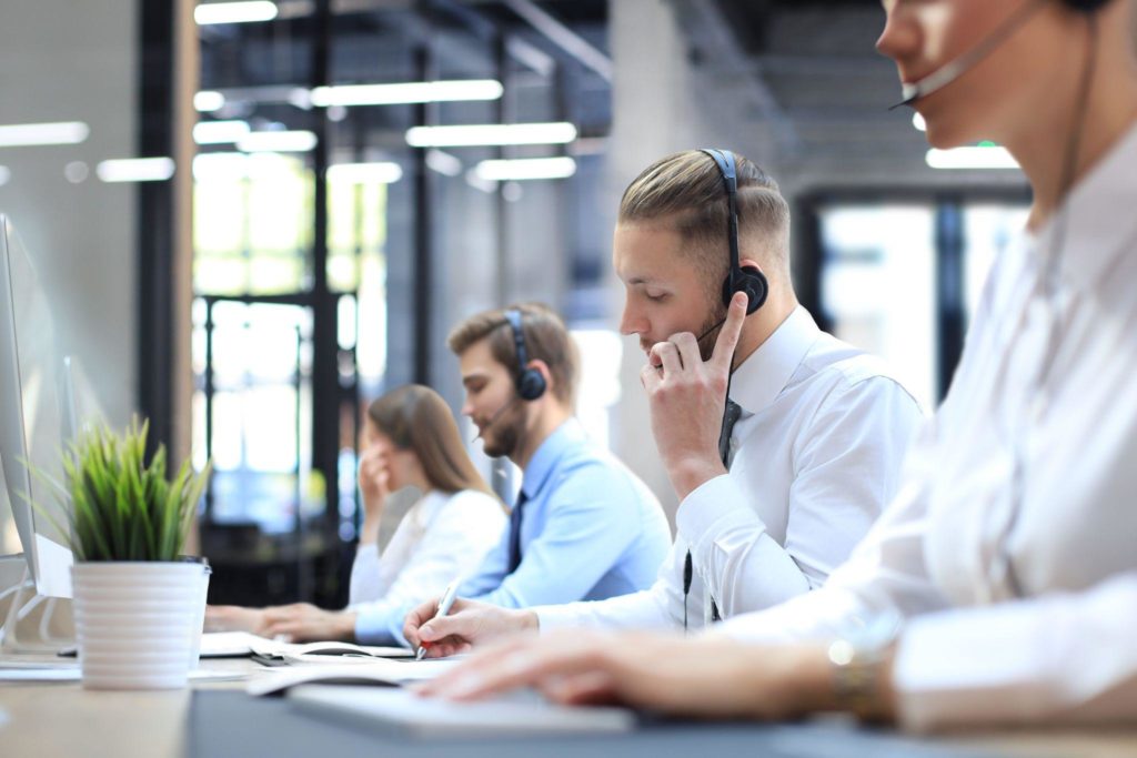 Portrait of call center worker accompanied by his team. Smiling customer support operator at work.