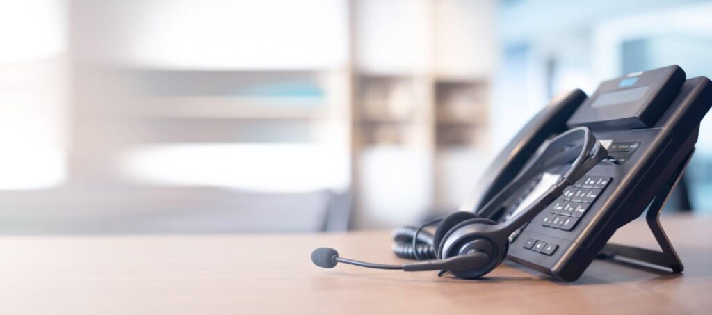 Business phone on a wooden desk with headset.