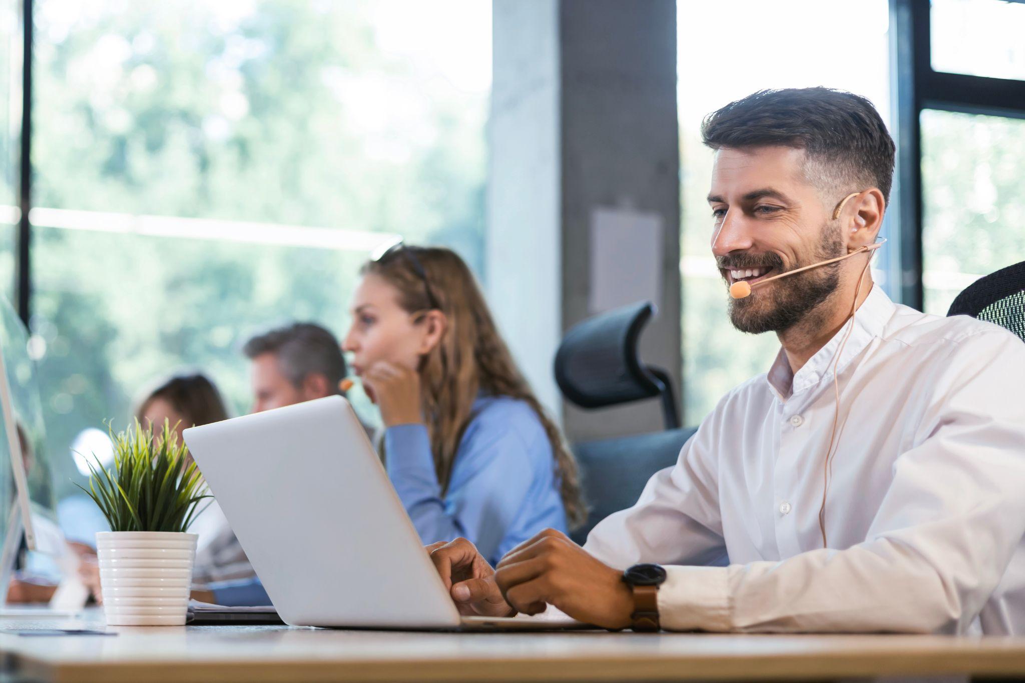 A man in a headset with laptop answers call professionally.