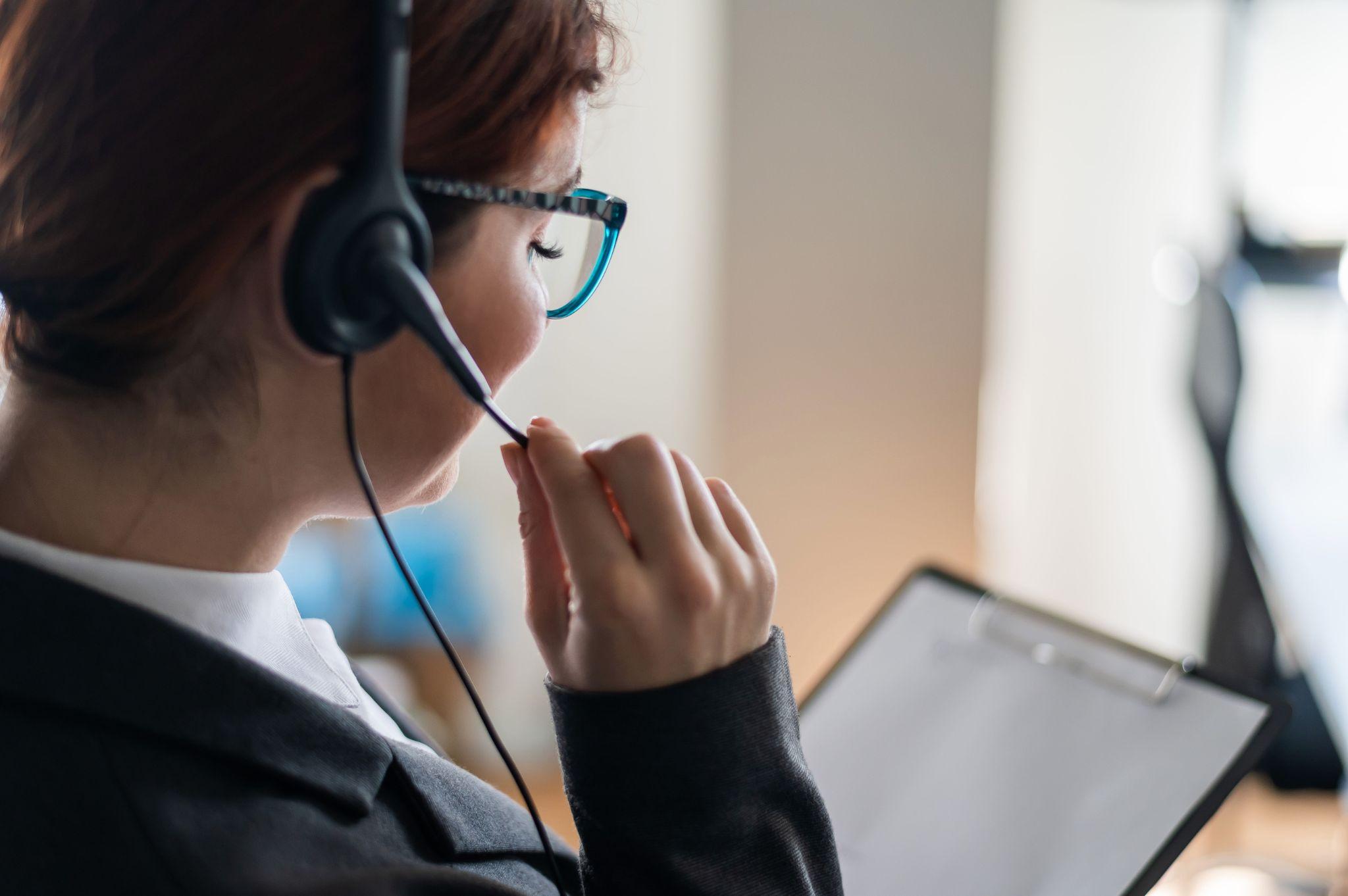 A professional speaks into a headset while reviewing notes, modeling how to answer the phone professionally.