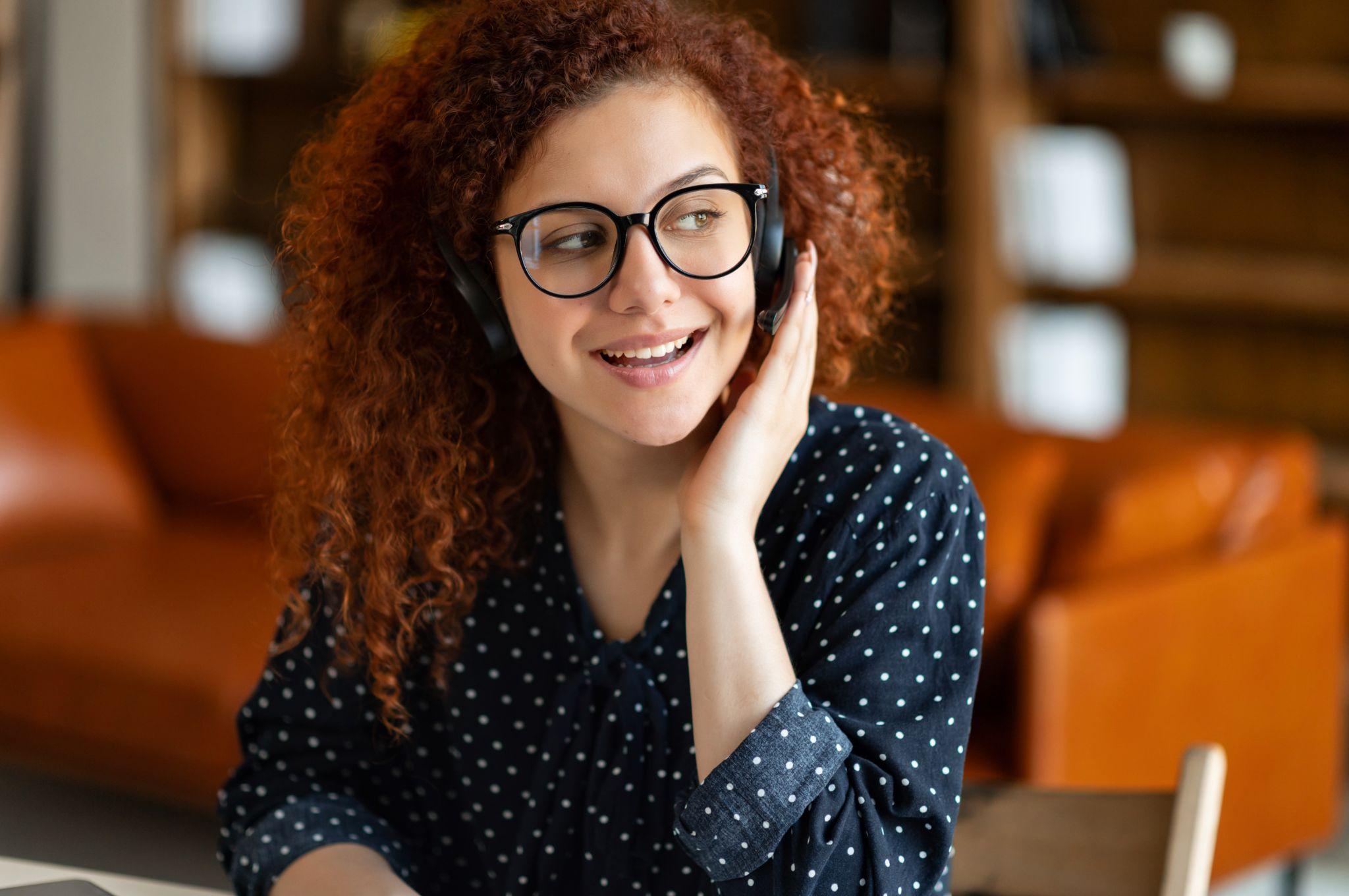 Close-up portrait of curly young businesswoman in a headset holding the microphone.