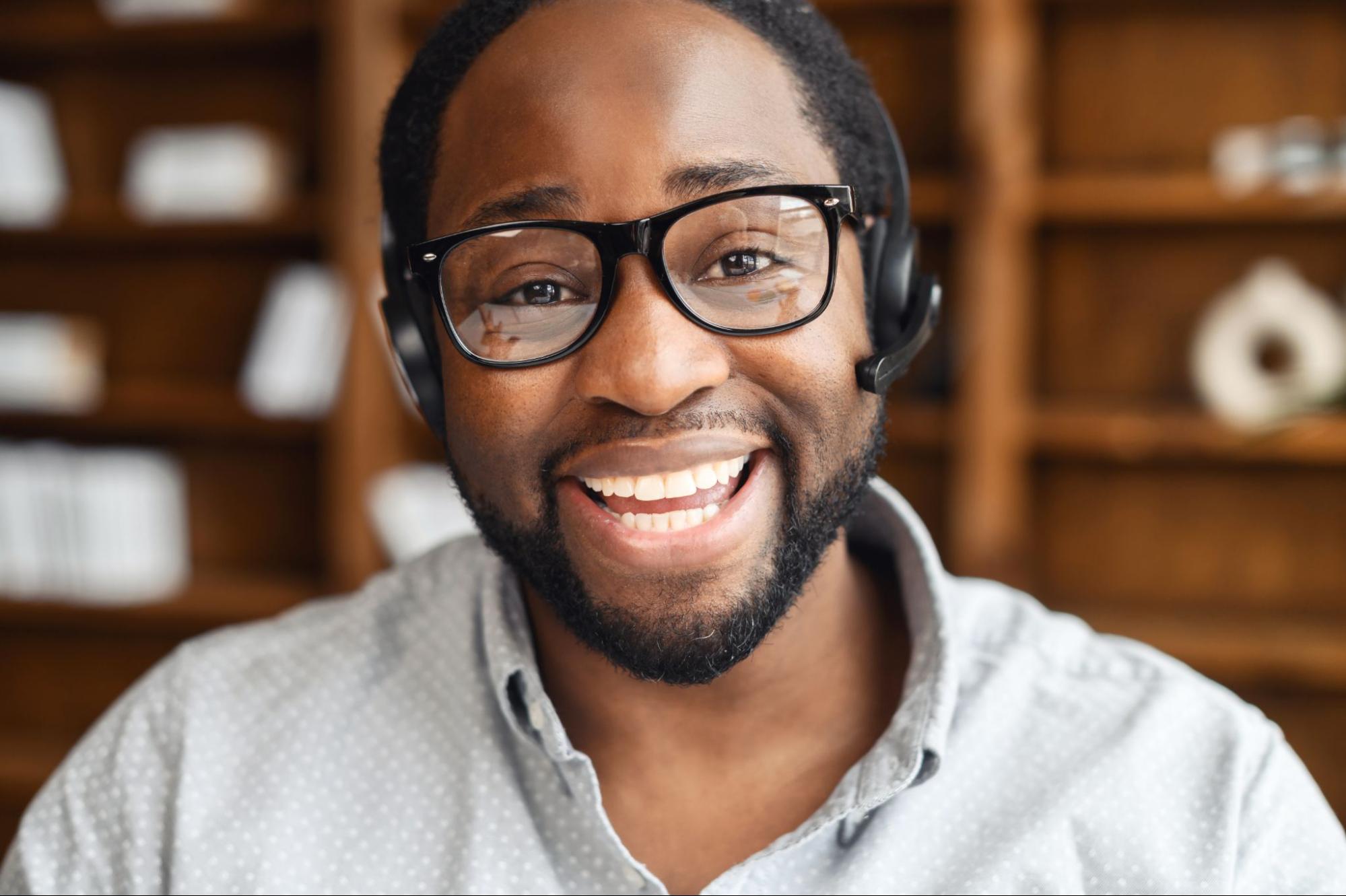 Smiling young African-American salesman in glasses and headset looking at the camera and laughing.