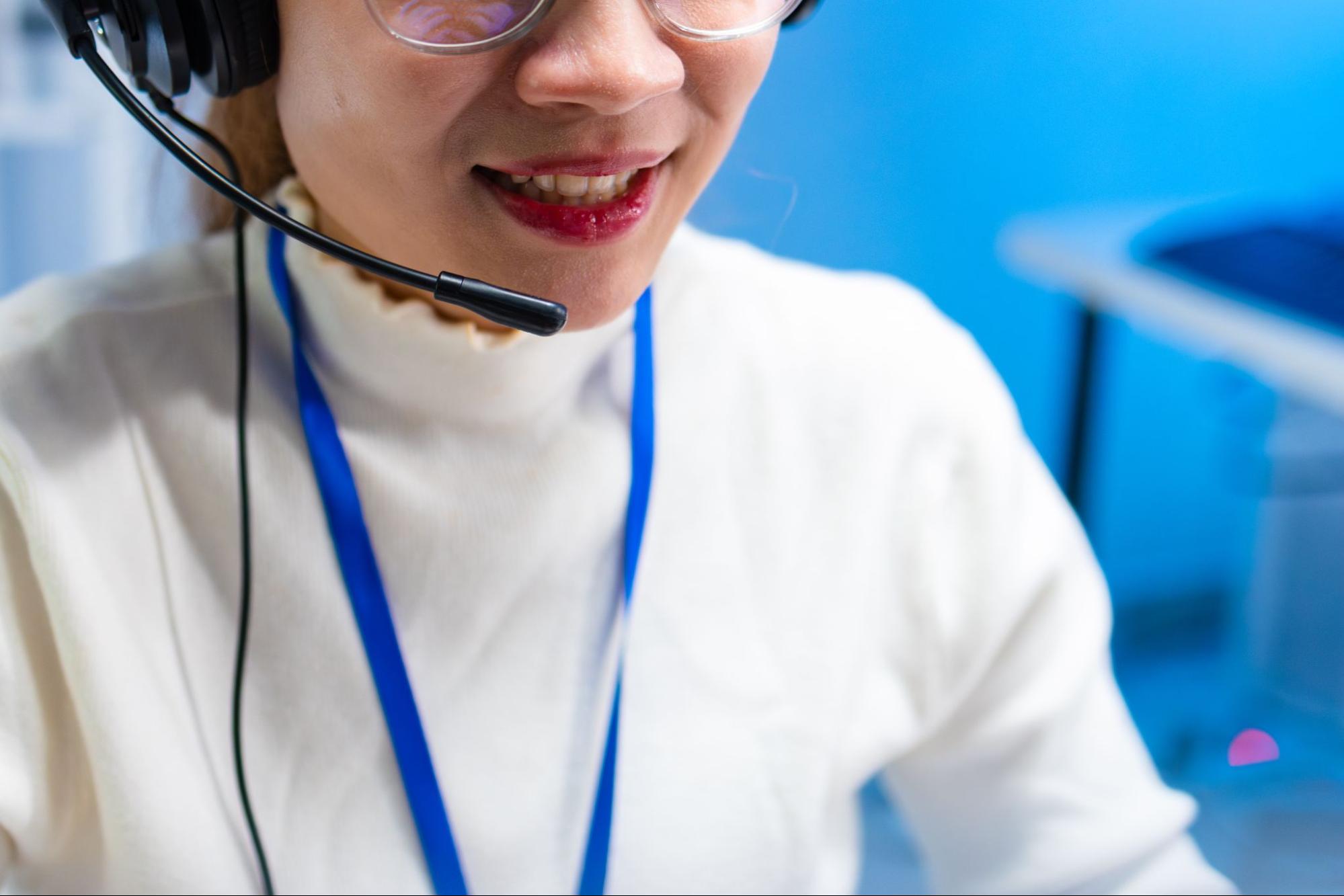 Female Customer Service Agent talking, typing and helping client via headset using computer in call center office.